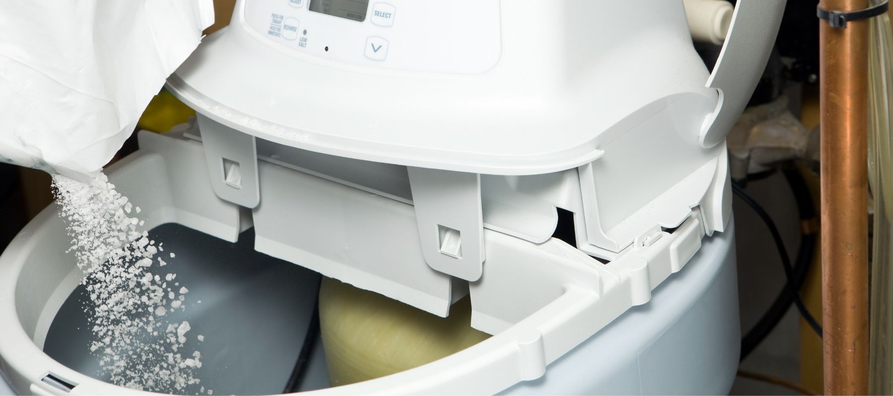 A person pours salt pellets from a white bag into the top of a water softener tank