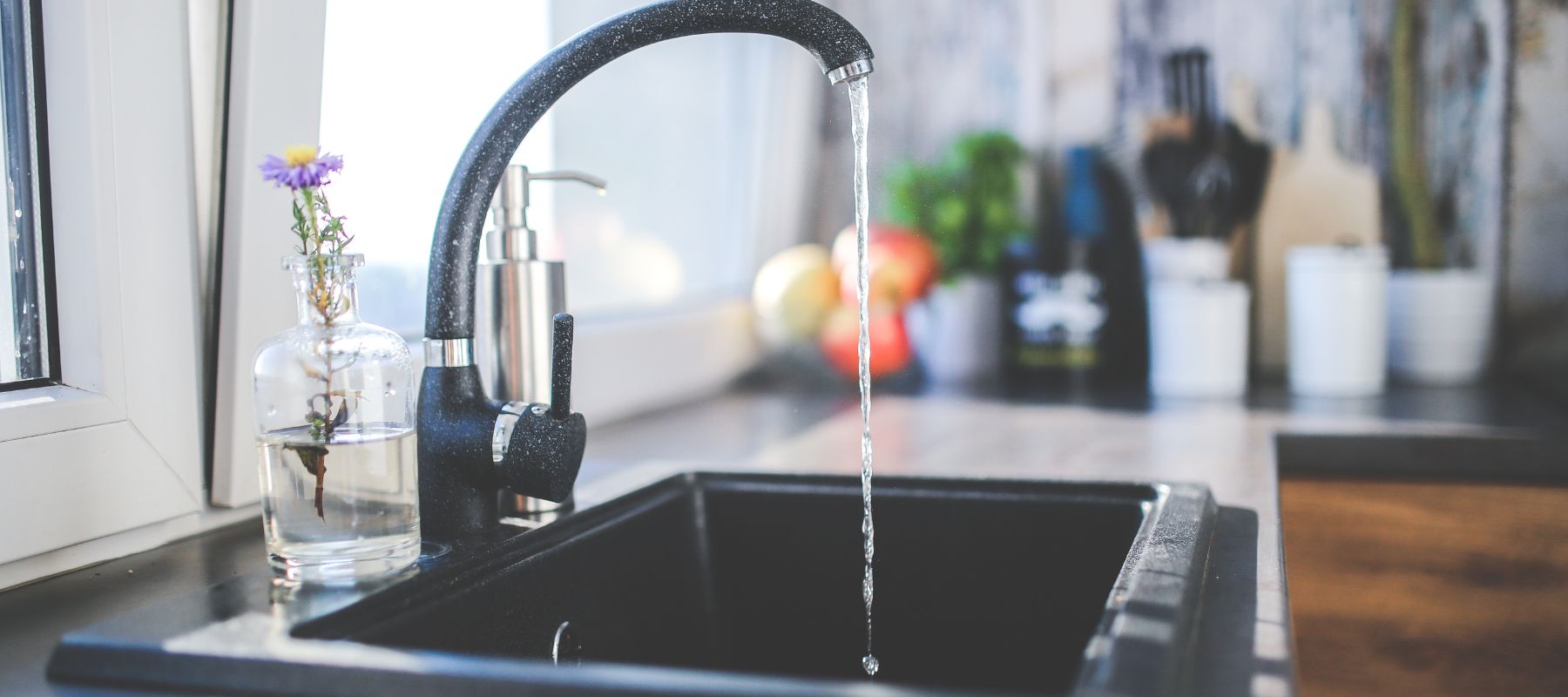 Water streams from a modern black faucet into a black sink, with a small vase holding a flower on the countertop