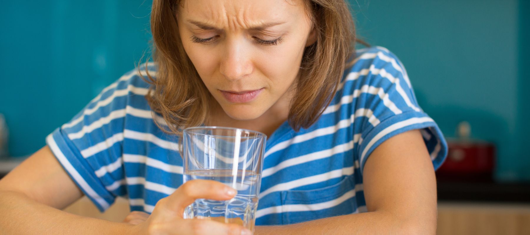 A woman with a concerned expression looks down into a glass of water she is holding