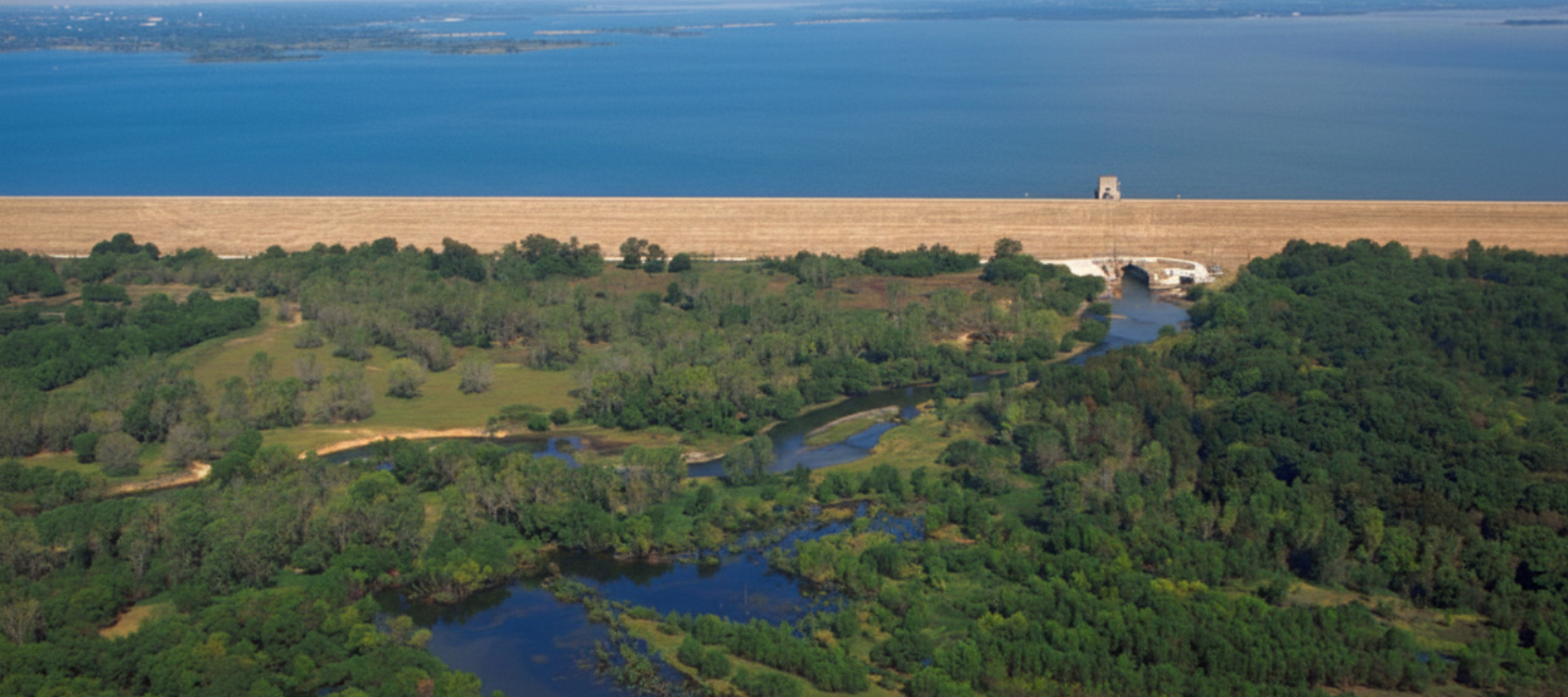 Aerial view of the Lewisville Lake dam and surrounding forest wetlands with the blue lake stretching to the horizon in Lewisville, TX.